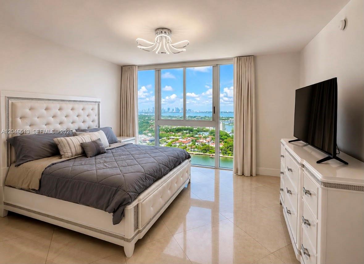 A bedroom features a white tufted bed, a dresser with a television, and floor-to-ceiling windows — 4775 Collins Ave # 2407, Miami Beach FL 33140, MIAMI BEACH, FL