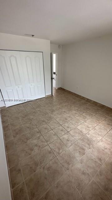 An empty bedroom features white walls, a white closet with double doors, and tiled flooring — MIAMI, FL