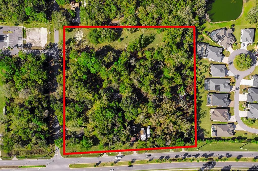 An aerial view shows a rectangular, tree-covered plot of land outlined in red — 4700 WARM SPRINGS AVENUE, WILDWOOD, FL