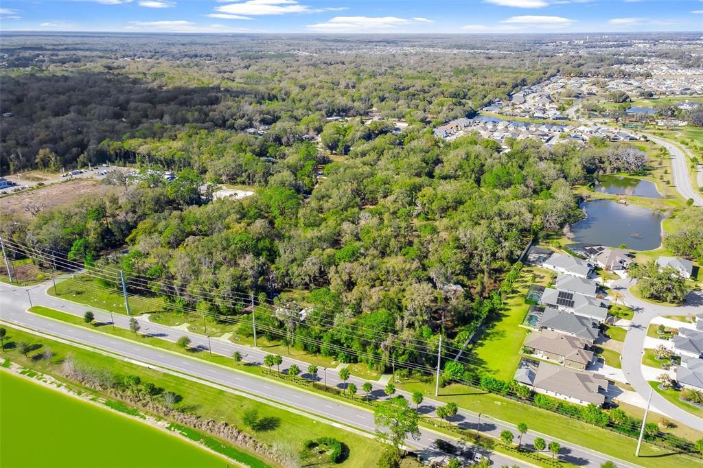 An aerial view shows a wooded lot bordered by a road, a pond, and residential homes — 4700 WARM SPRINGS AVENUE, WILDWOOD, FL