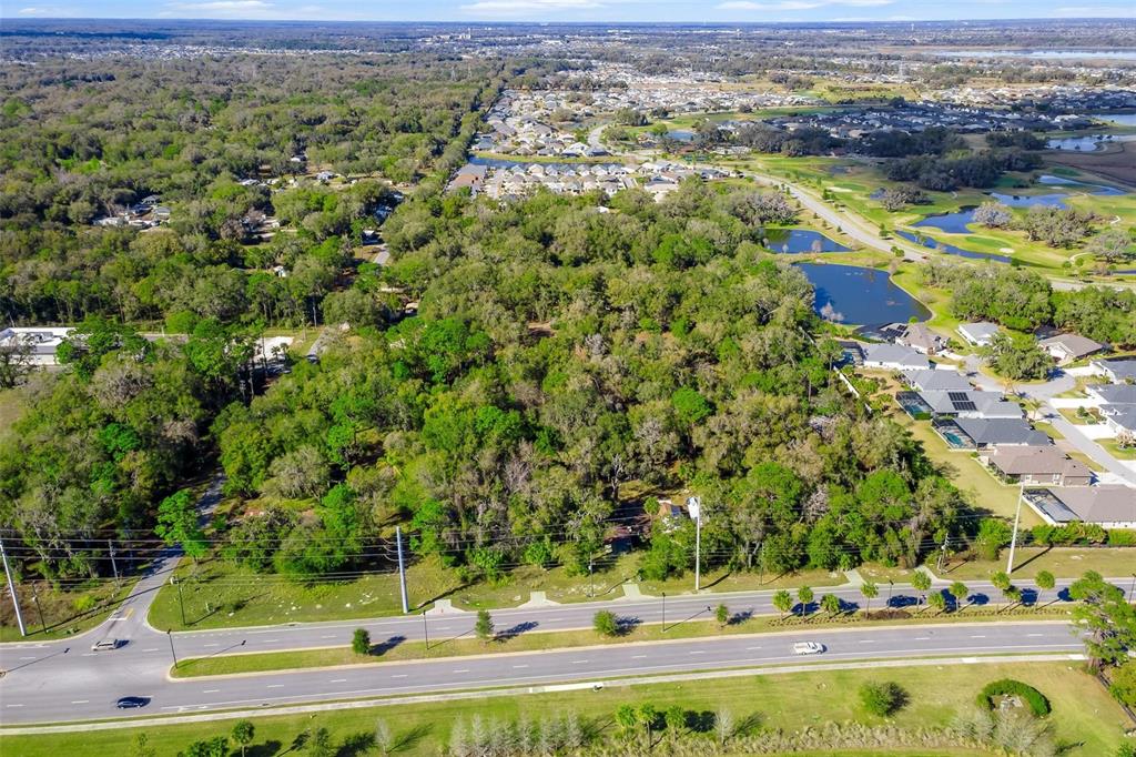 An aerial view shows a large, wooded lot situated between a road and a residential neighborhood — 4700 WARM SPRINGS AVENUE, WILDWOOD, FL