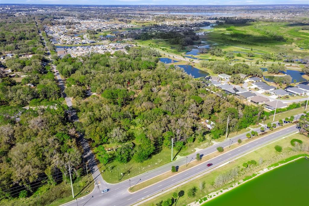 An aerial view shows a wooded lot bordered by a road, residential homes, and ponds — 4700 WARM SPRINGS AVENUE, WILDWOOD, FL