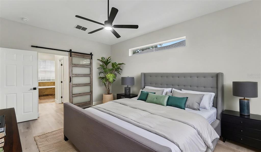 A bedroom features a gray tufted bed, a sliding barn door, and a ceiling fan — 1612 FOREST HILLS LANE, HAINES CITY, FL