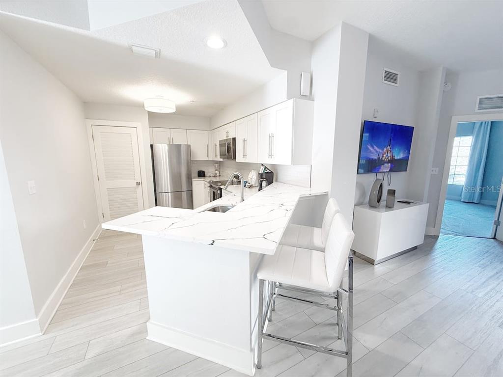 A modern kitchen features white cabinets, marble-patterned countertops, stainless steel appliances, and two bar stools — 8762 WORLDQUEST BOULEVARD UNIT 6205, ORLANDO, FL