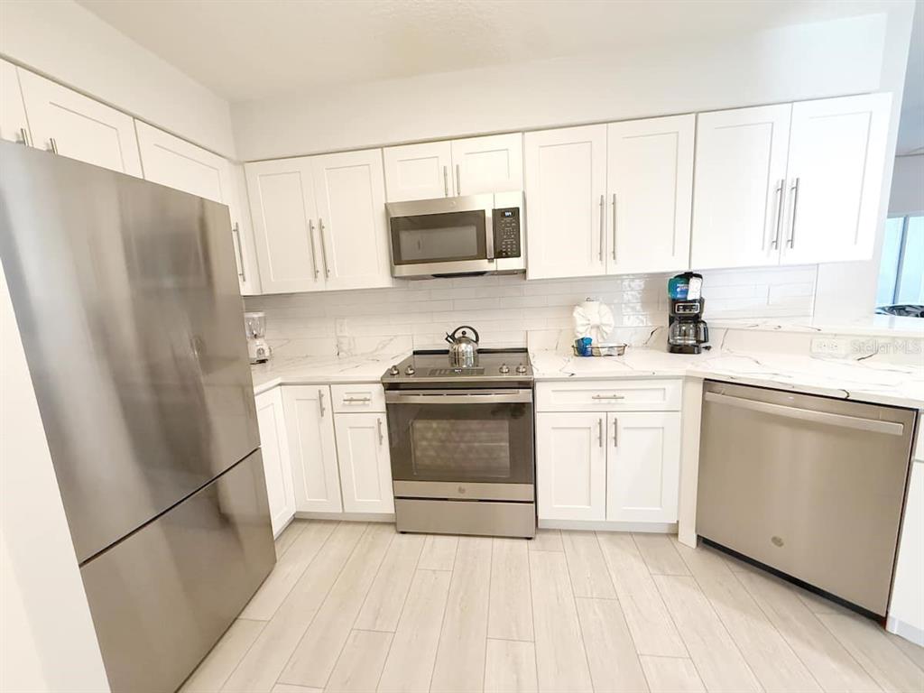 A kitchen features white cabinets, stainless steel appliances, and light-colored tile flooring — 8762 WORLDQUEST BOULEVARD UNIT 6205, ORLANDO, FL