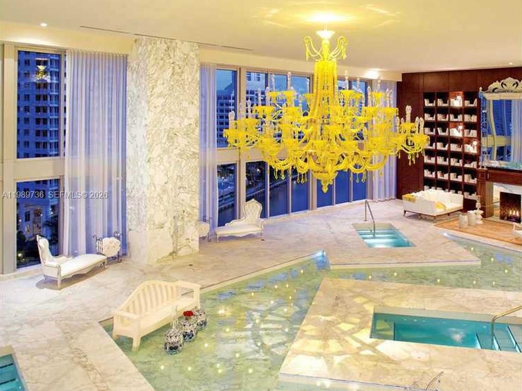 A luxurious indoor pool room features a large yellow chandelier, marble floors, and floor-to-ceiling windows — 475 Brickell Ave # 5111, Miami FL 33131, MIAMI, FL