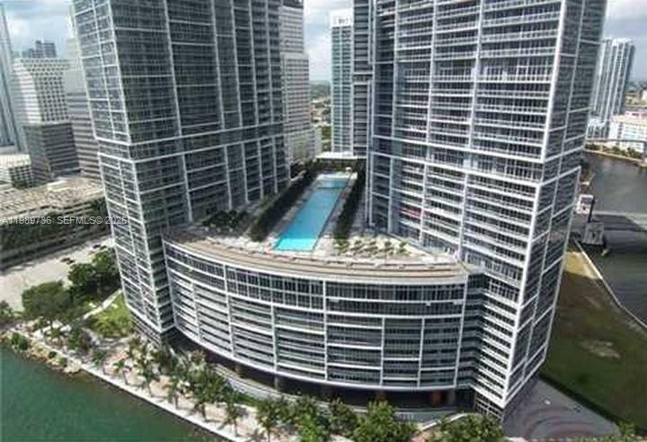 An aerial view shows the exterior of a modern high-rise building with a rooftop pool — 475 Brickell Ave # 5111, Miami FL 33131, MIAMI, FL