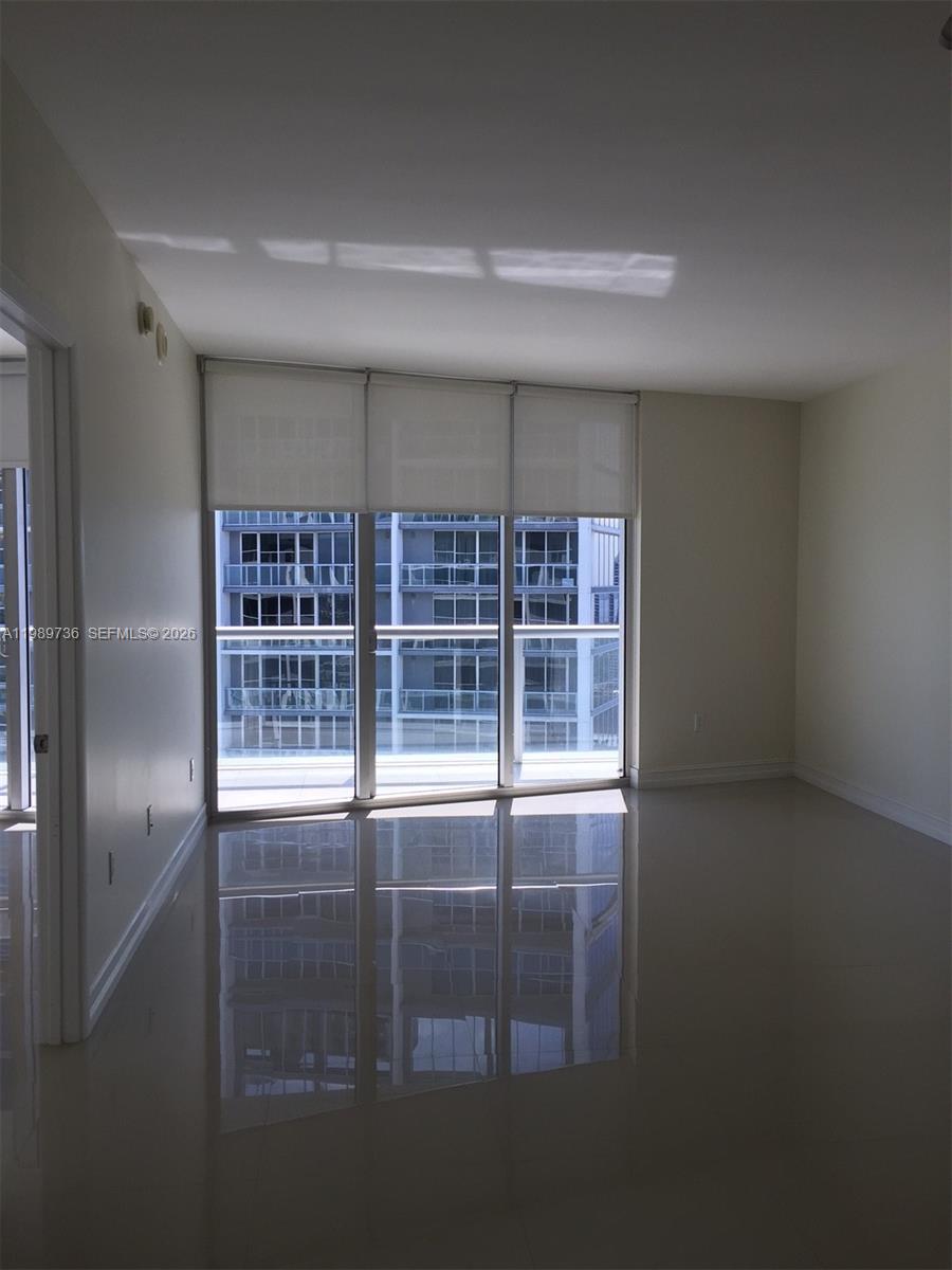 An empty room with light-colored tile flooring, white walls, and large windows overlooking a building — 475 Brickell Ave # 5111, Miami FL 33131, MIAMI, FL