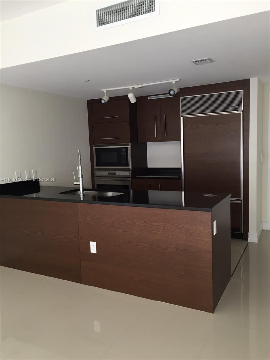 A modern kitchen features dark wood cabinetry, a black countertop island, and stainless steel appliances — 475 Brickell Ave # 5111, Miami FL 33131, MIAMI, FL
