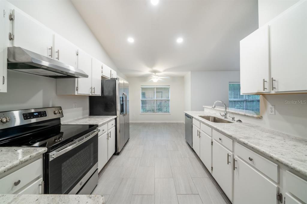 A kitchen features white cabinets, granite countertops, stainless steel appliances, and light gray tile flooring — 7136 SW 81ST DRIVE, GAINESVILLE, FL