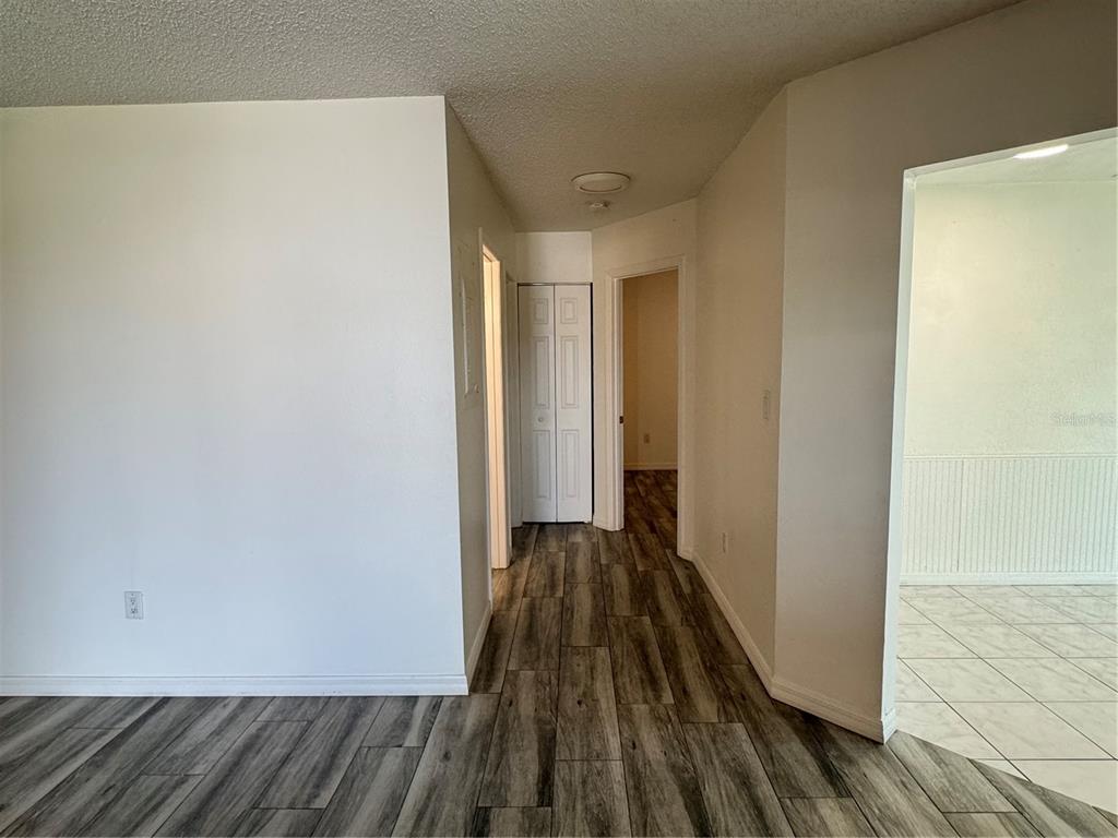 A hallway with wood-look flooring leads to a closet and a room beyond — 215 FERNWOOD ST, LEESBURG, FL