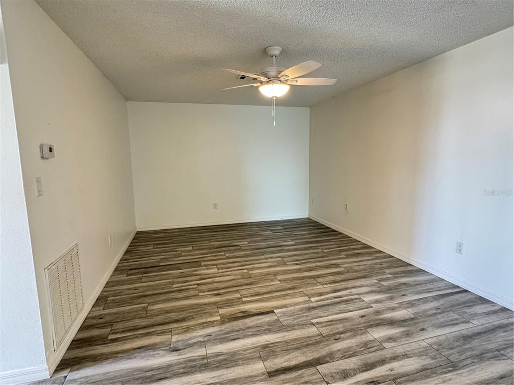 An empty room features wood-look plank flooring, white walls, and a ceiling fan — 215 FERNWOOD ST, LEESBURG, FL