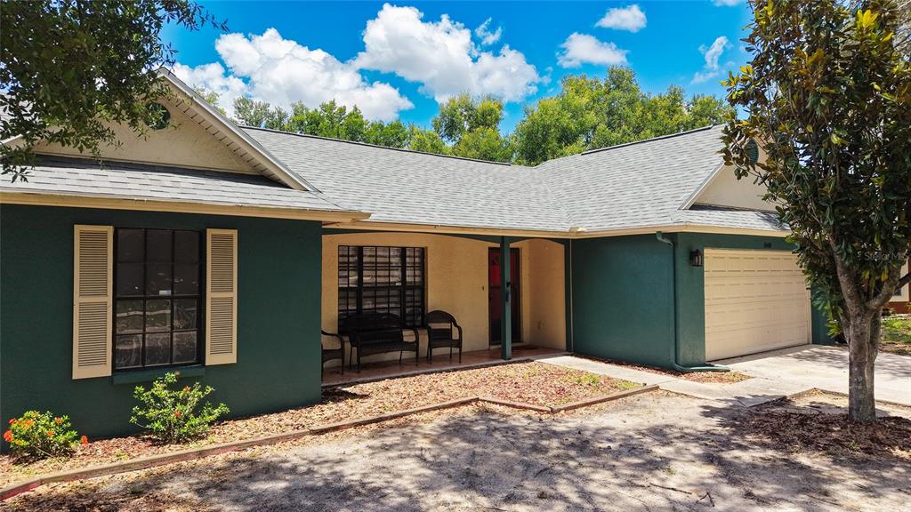 The exterior of a single-story house features a covered porch, dark green siding, and a red door — 1048 MALLETWOOD DRIVE, BRANDON, FL