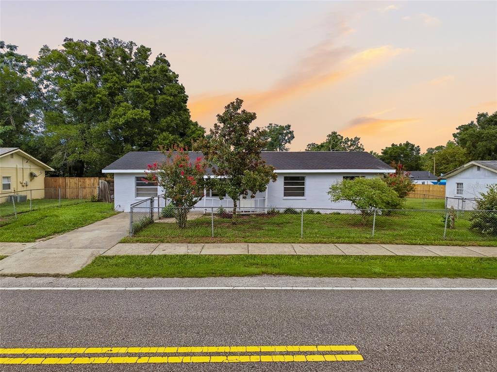A single-story white house with a fenced front yard sits behind a paved road — 6376 CAMMIE STREET, BROOKSVILLE, FL