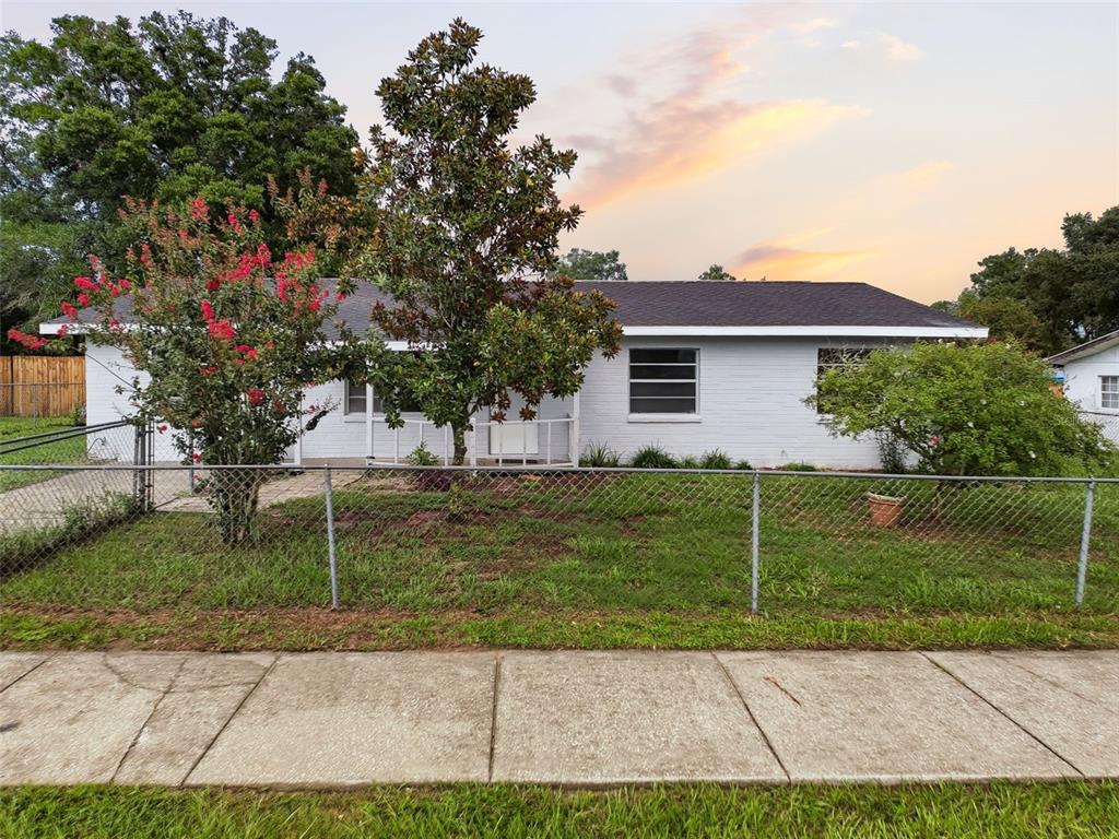 A single-story white brick house with a chain-link fence and trees in the front yard — 6376 CAMMIE STREET, BROOKSVILLE, FL