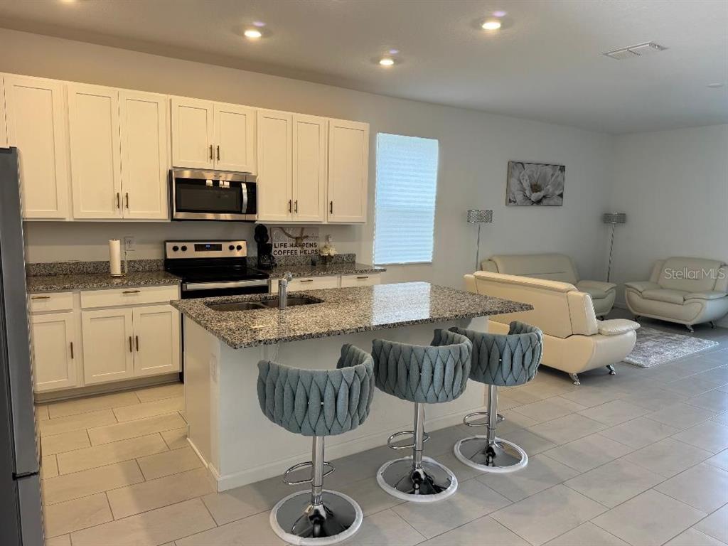 A kitchen with white cabinets, granite countertops, and three blue bar stools at an island — 441 SILVER PALM DRIVE, HAINES CITY, FL