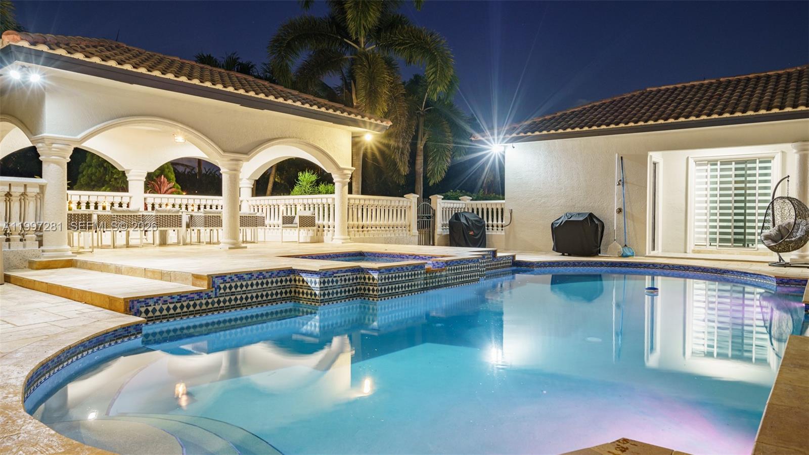 A swimming pool with an integrated spa sits in front of a covered patio area — 13751 Pine Meadow Ct, Davie FL 33325, DAVIE, FL