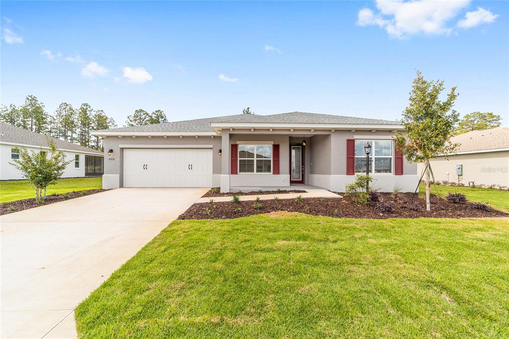 A single-story suburban house with a two-car garage, gray stucco exterior, and red shutters — 10710 SW 104TH PLACE, OCALA, FL