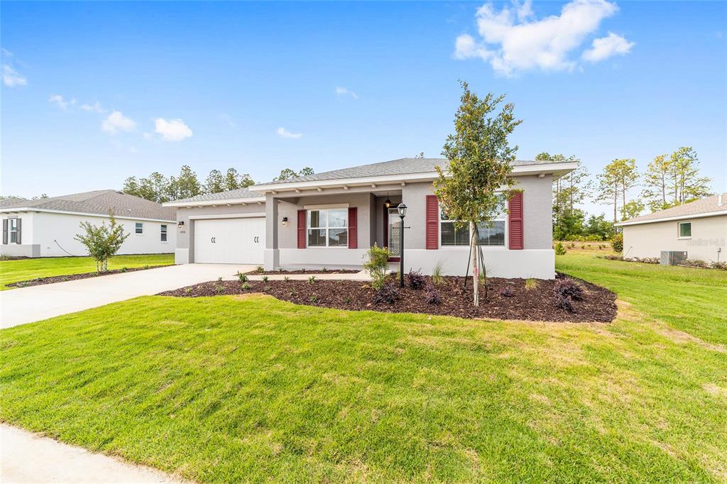 A single-story suburban house with a gray stucco exterior, red shutters, and a two-car garage — 10710 SW 104TH PLACE, OCALA, FL