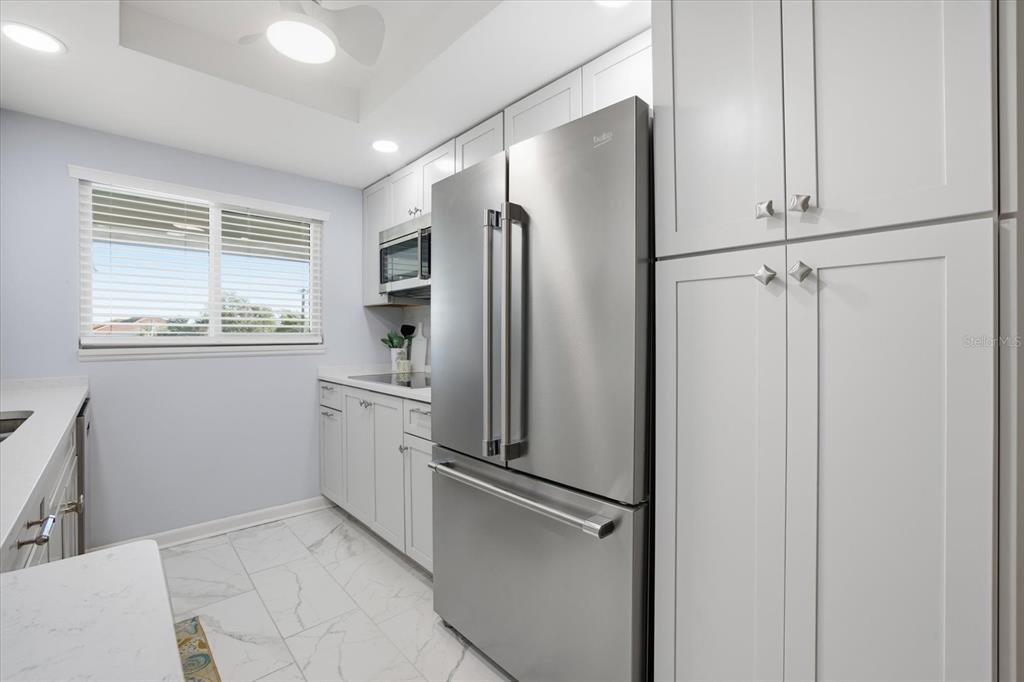 A bright kitchen features white shaker cabinets, quartz countertops, a herringbone backsplash, and marble-look flooring — 649 TAMIAMI TRAIL S UNIT 306, VENICE, FL