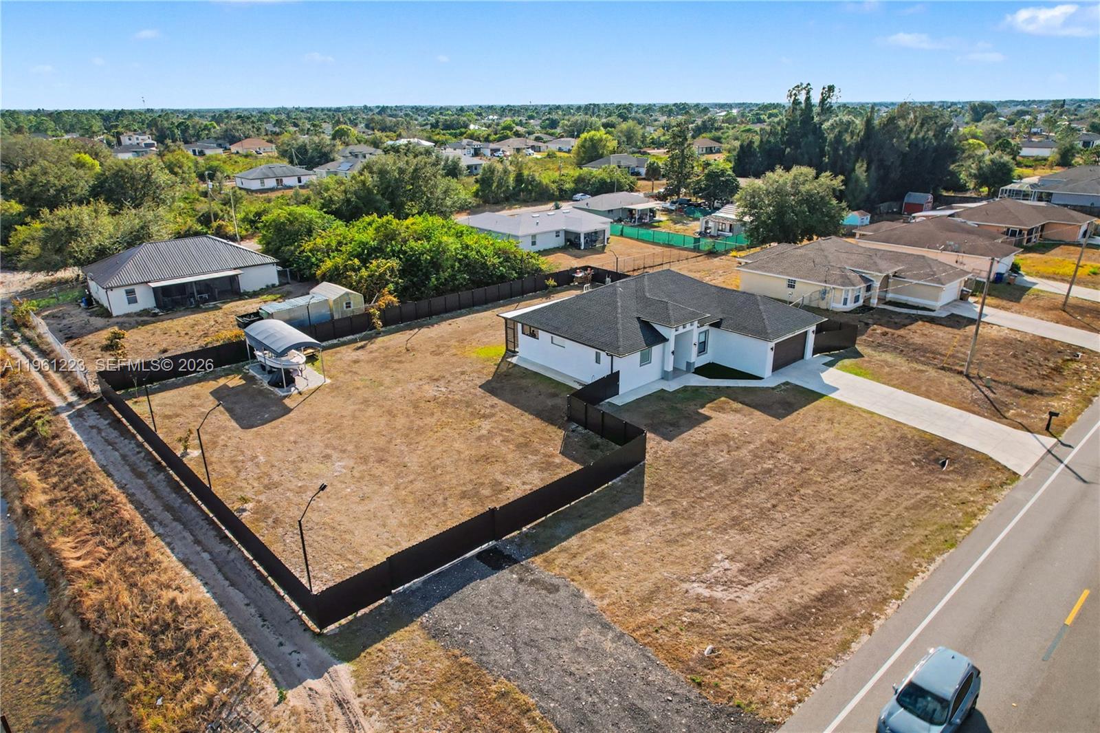 An aerial view shows a white house with a dark roof and a fenced yard — 3705 SW 23rd St, Lehigh Acres FL 33976, LEHIGH ACRES, FL