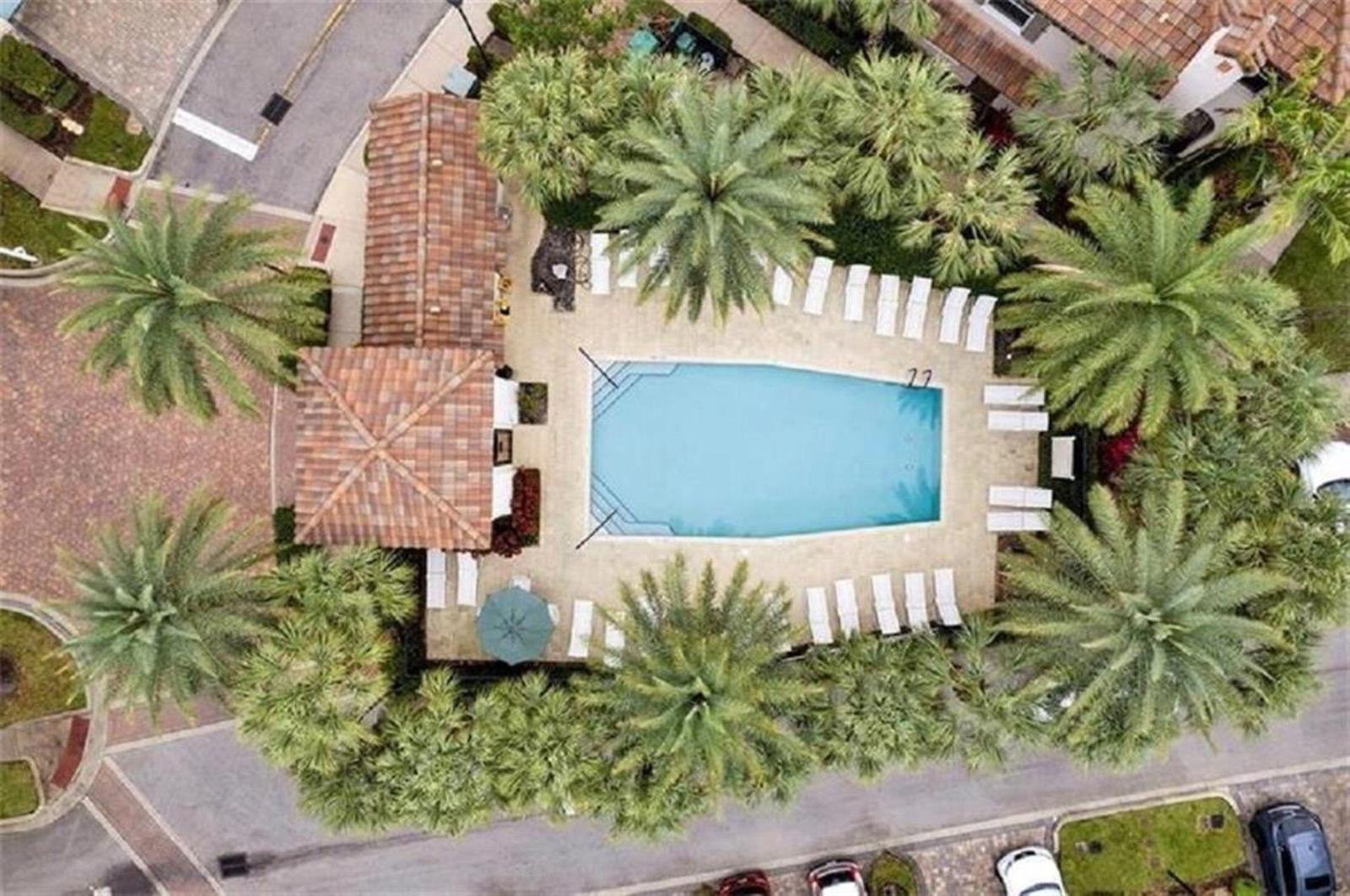 An aerial view shows a swimming pool surrounded by lounge chairs, palm trees, and buildings — 2930 Cascada Isles Way, Cooper City FL 33024, COOPER CITY, FL