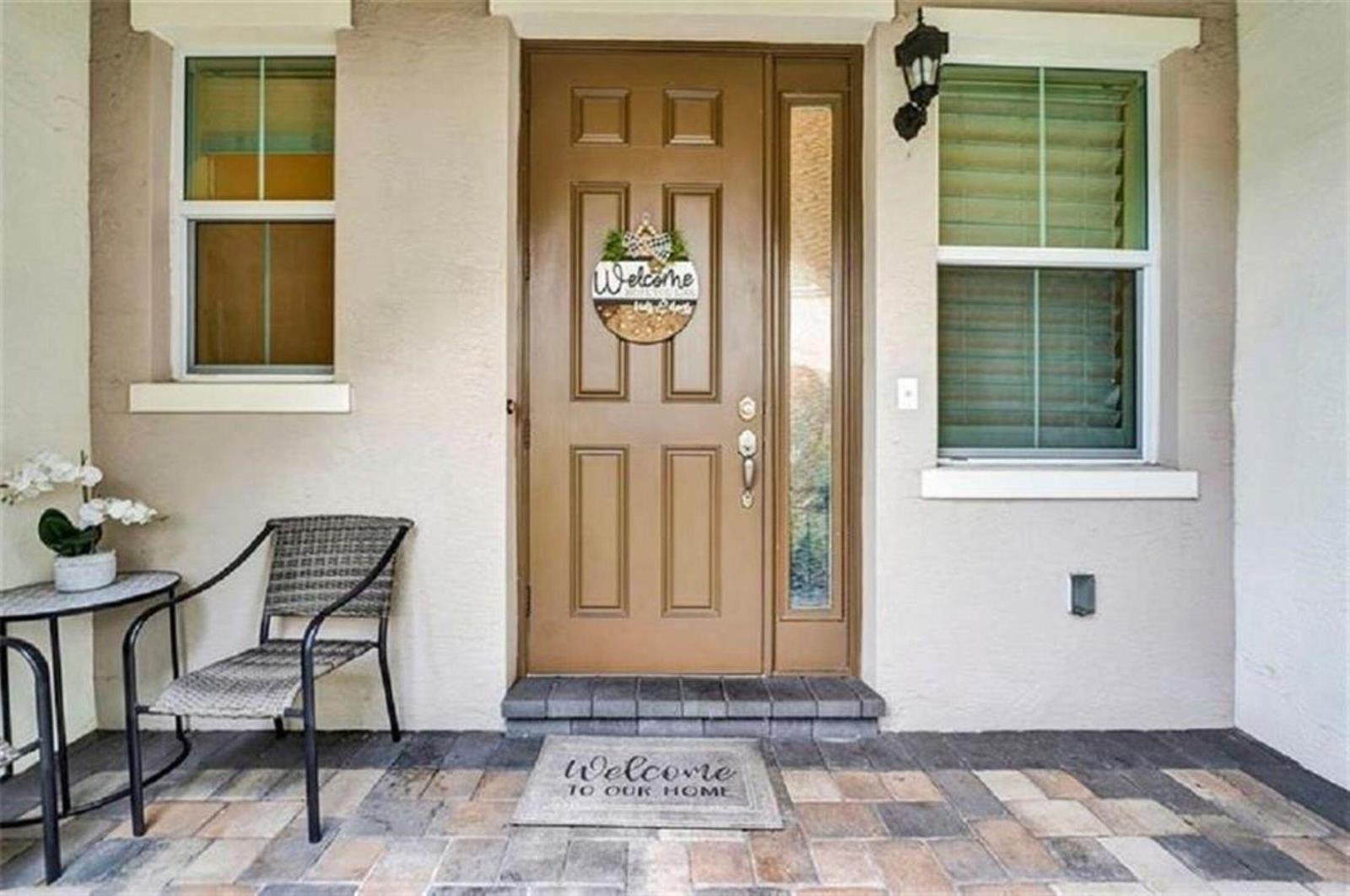 A front porch features a brown door with a sidelight, a chair, and a welcome mat — 2930 Cascada Isles Way, Cooper City FL 33024, COOPER CITY, FL