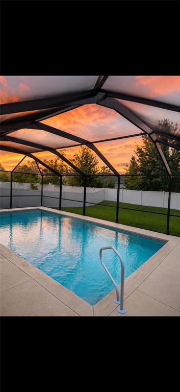 A rectangular swimming pool sits inside a screened-in lanai at sunset — 2016 ROSEWOOD CIRCLE, LAKELAND, FL
