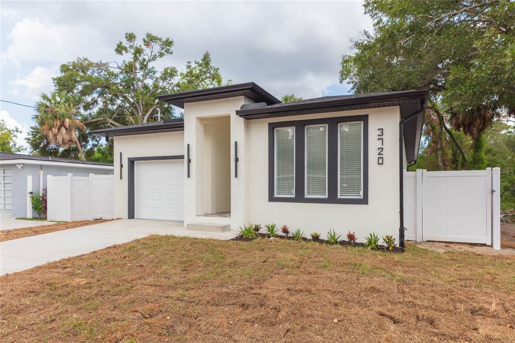 A modern, single-story house with white stucco walls, a dark roof, and a concrete driveway — 3720 N 32ND, TAMPA, FL
