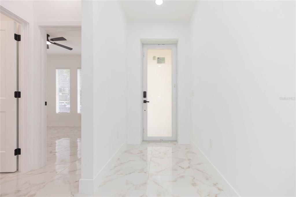 A bright hallway with white walls and light-colored marble-patterned tile flooring leads to a door — 3720 N 32ND, TAMPA, FL