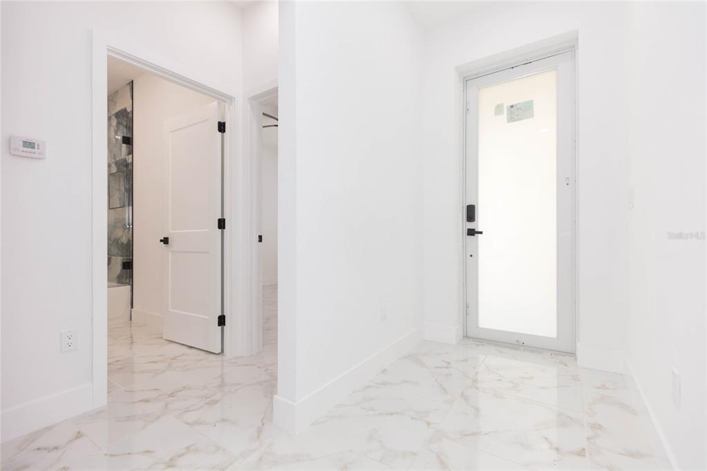 A bright hallway with white walls, marble-look tile floors, and a glass-paneled exterior door — 3720 N 32ND, TAMPA, FL