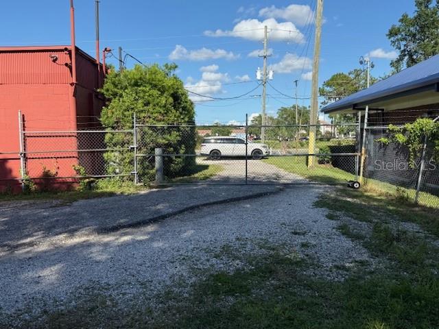 A gravel driveway leads to a chain-link gate beside a red building and a roofed structure — 644 MAGUIRE ROAD, OCOEE, FL
