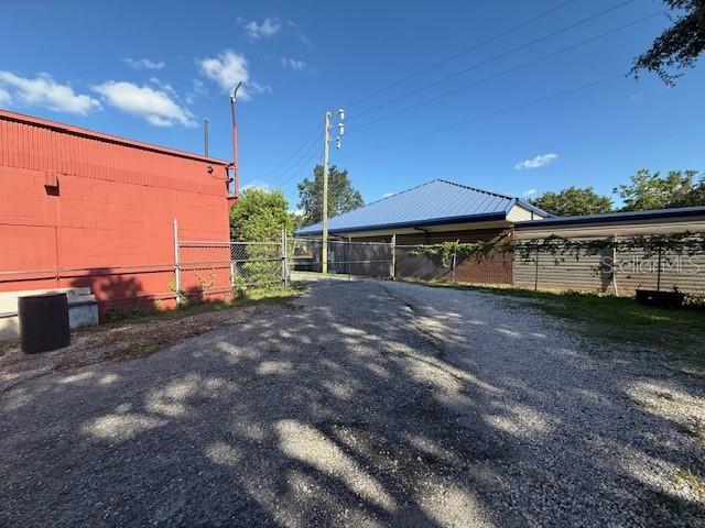 A gravel driveway sits between a red metal building and a blue-roofed structure — 644 MAGUIRE ROAD, OCOEE, FL