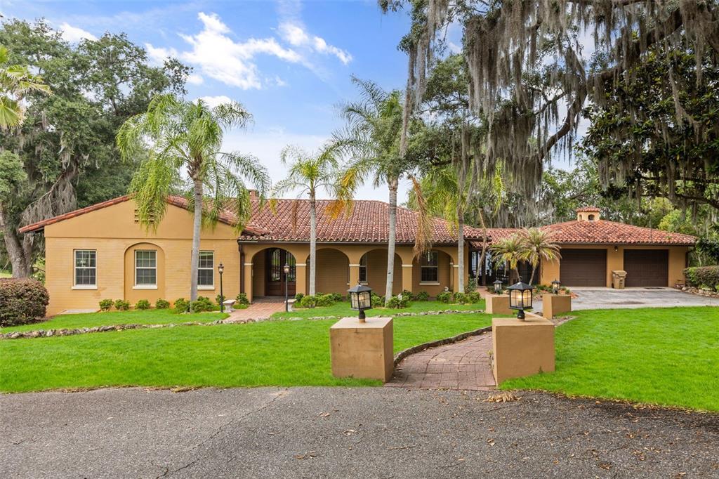 A single-story tan stucco house with a red tile roof and an attached two-car garage — 1909 COUNTRY CLUB DRIVE, EUSTIS, FL