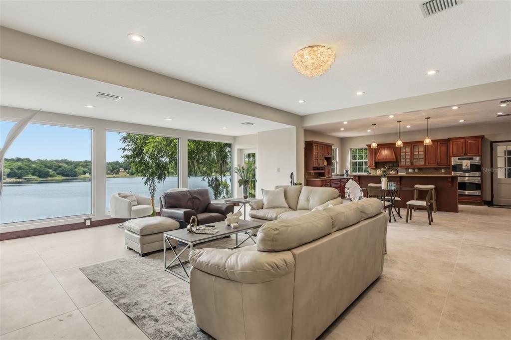 A spacious open-concept living room and kitchen area features large windows overlooking a lake — 1909 COUNTRY CLUB DRIVE, EUSTIS, FL