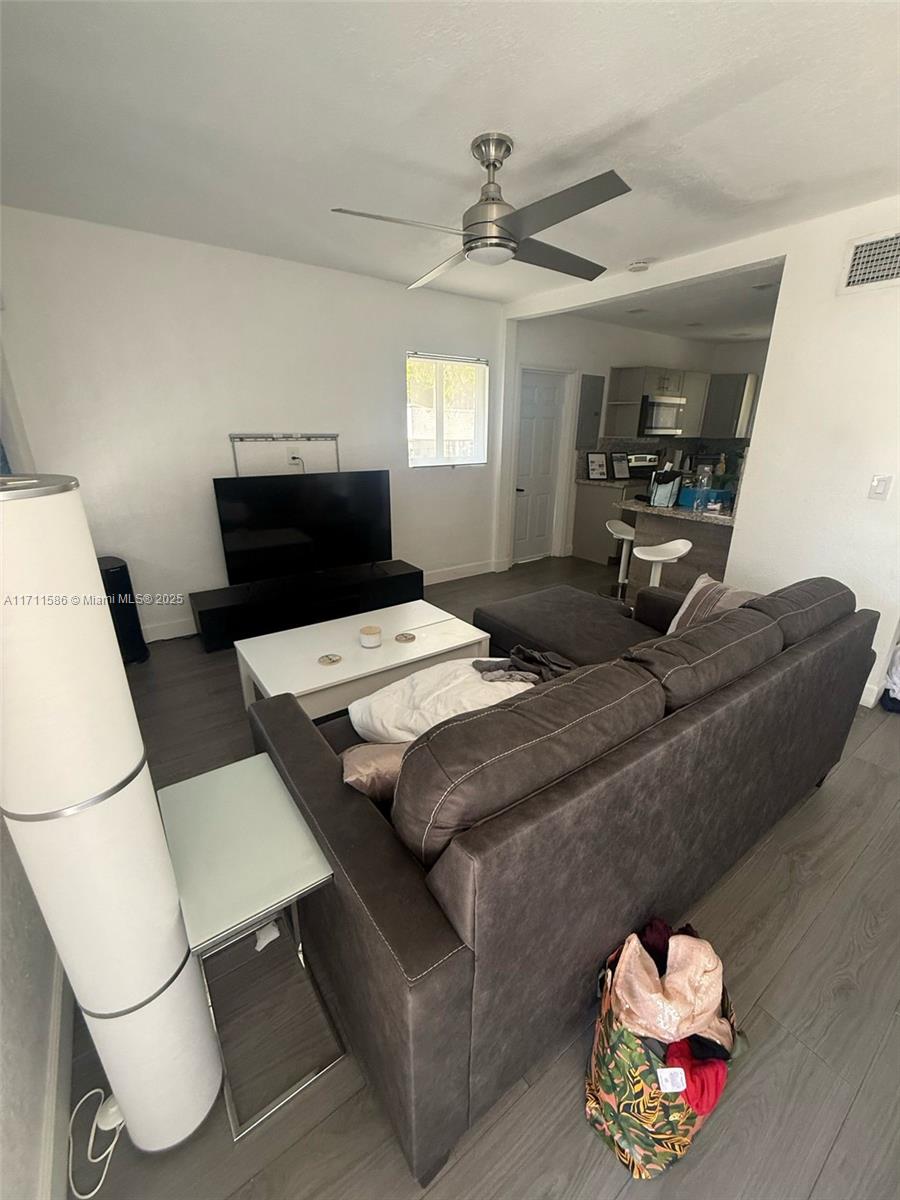 A living room with gray flooring, a sectional sofa, and an adjacent kitchen area — 241 NW 34th Ter, Miami FL 33127, MIAMI, FL