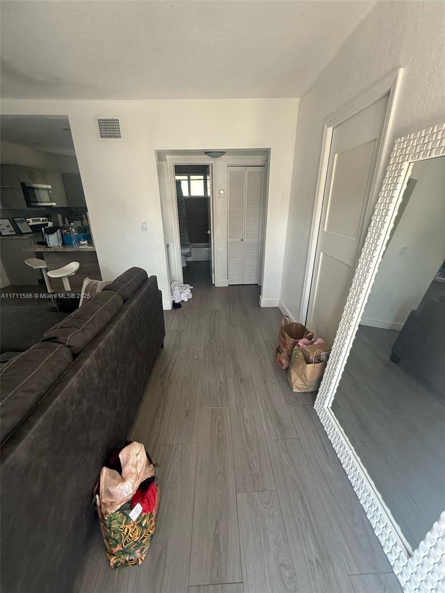 A living room with gray wood-look flooring leads to a hallway with a bathroom — 241 NW 34th Ter, Miami FL 33127, MIAMI, FL