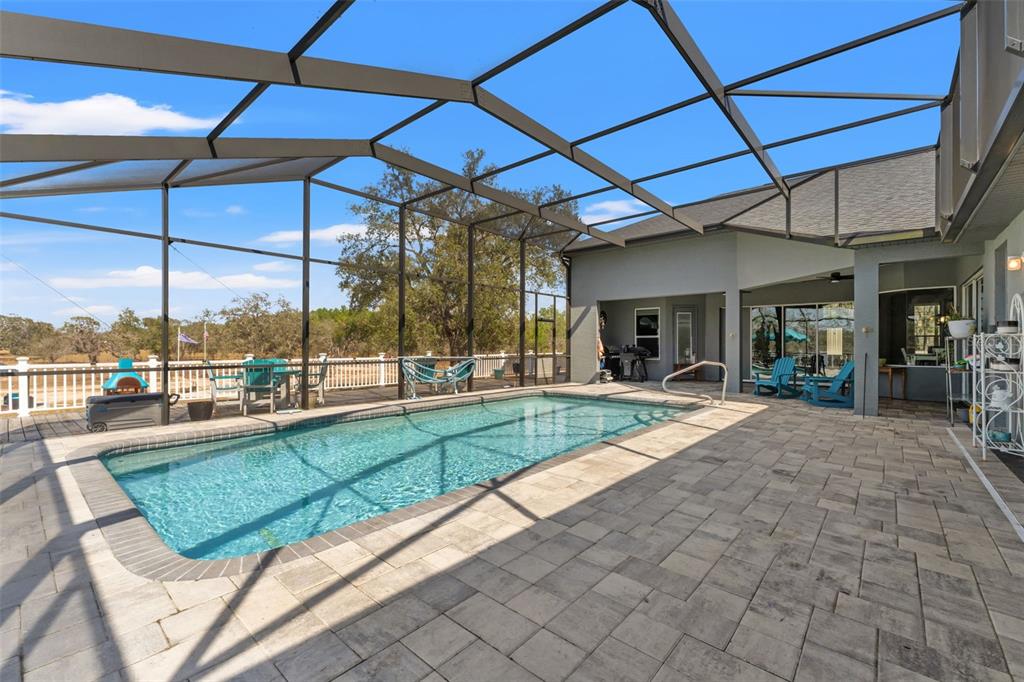 A rectangular swimming pool sits on a paved patio enclosed by a large screen cage — 12277 ESKIMO CURLEW ROAD, WEEKI WACHEE, FL