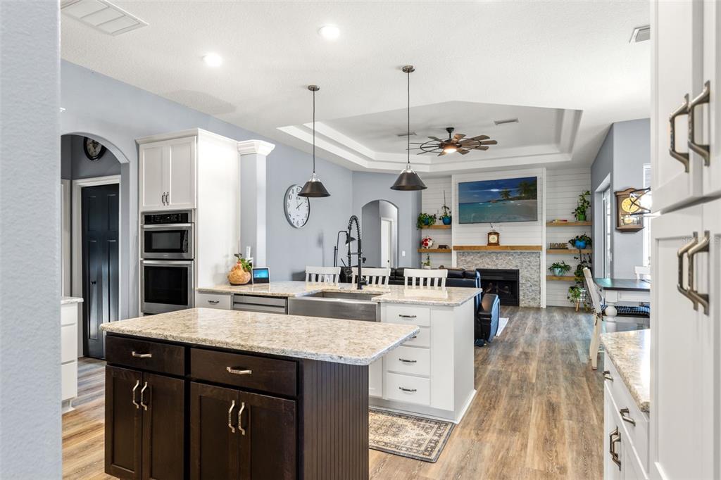 A kitchen with a dark wood island, white cabinets, granite countertops, and an adjacent living area — 12277 ESKIMO CURLEW ROAD, WEEKI WACHEE, FL