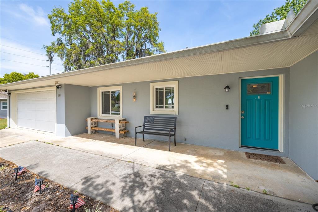 A gray house exterior features a teal front door, a garage, and a metal bench — 1709 UMBRELLA TREE DRIVE, EDGEWATER, FL
