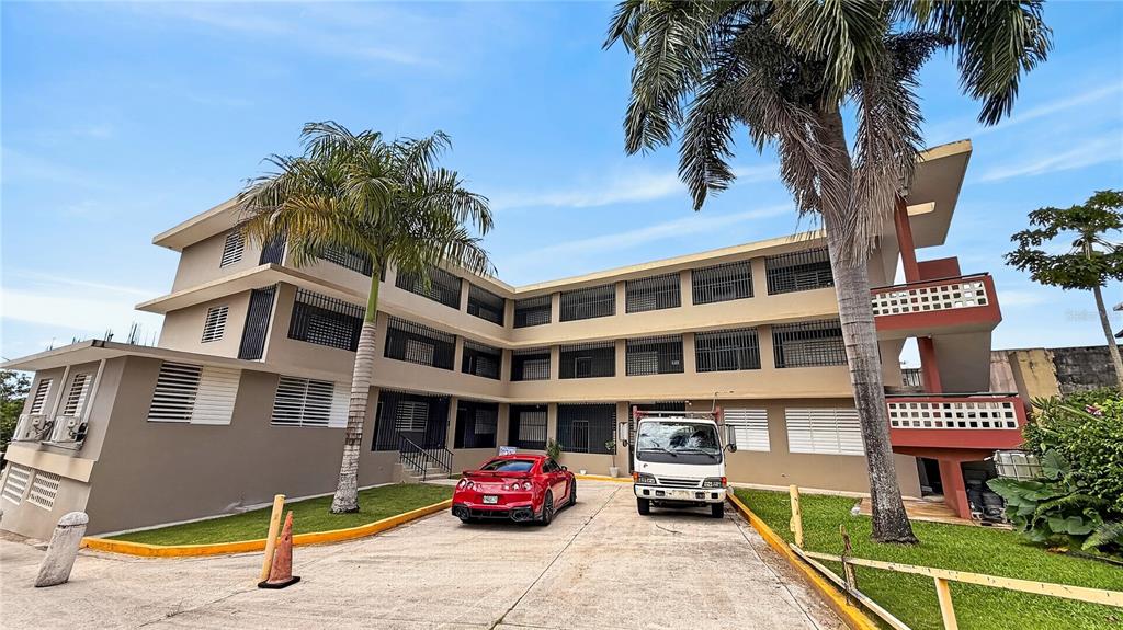 A three-story apartment building with a red sports car and a white truck parked outside — 120 BO HATO TEJAS, BAYAMON, PR