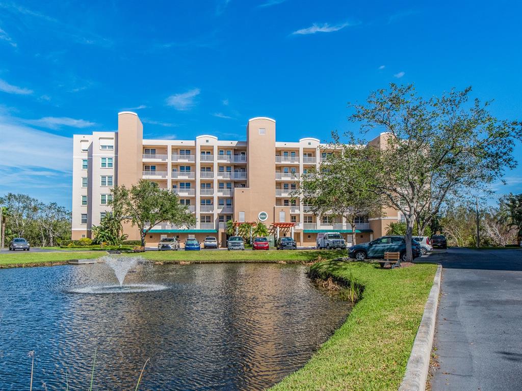 A multi-story tan apartment building stands behind a pond with a fountain and parking lot — 6550 SHORELINE DRIVE UNIT 7502, ST PETERSBURG, FL