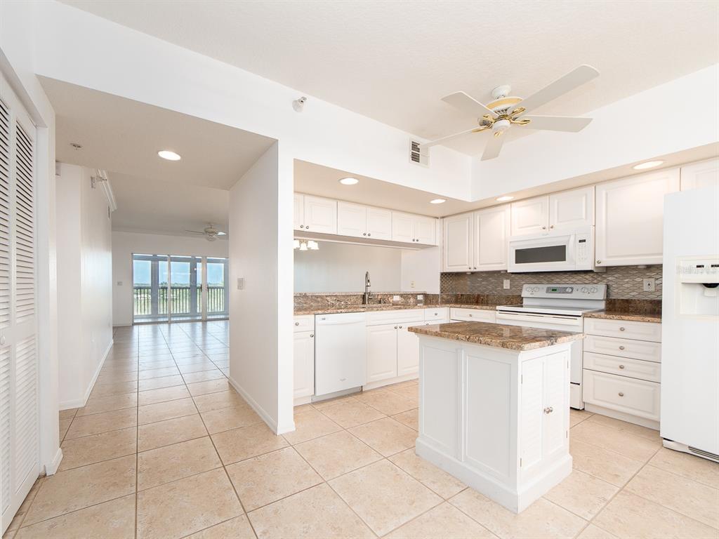 A kitchen with white cabinets, granite countertops, and a center island, adjacent to a hallway — 6550 SHORELINE DRIVE UNIT 7502, ST PETERSBURG, FL