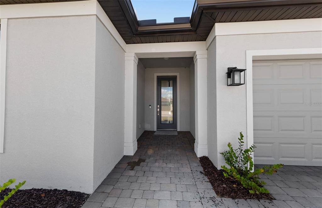 The exterior entrance features a paved walkway leading to a dark-framed glass front door — 1626 PEPPER GRASS DRIVE SW, NORTH PORT, FL