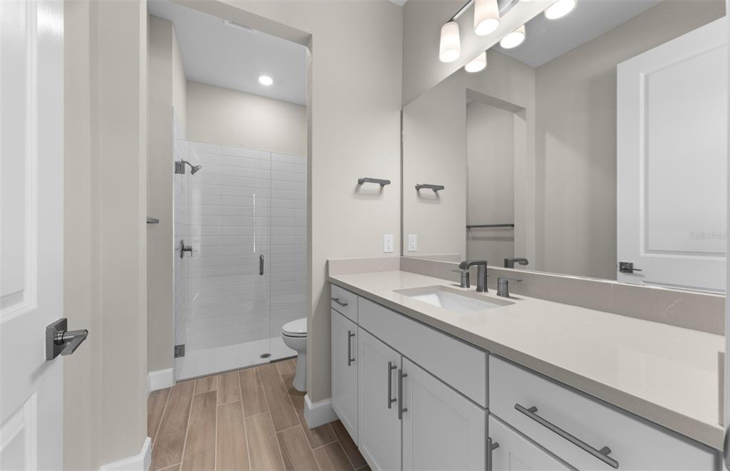 A modern bathroom features a white vanity, a glass-enclosed shower, and wood-look tile flooring — 1626 PEPPER GRASS DRIVE SW, NORTH PORT, FL