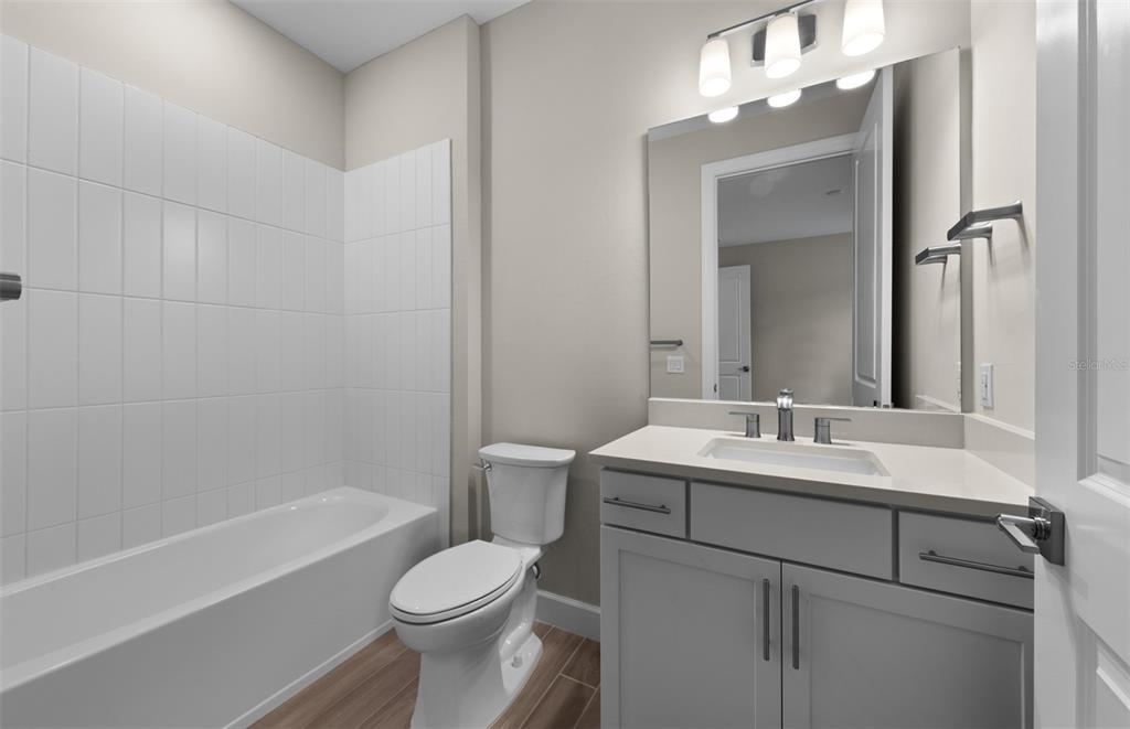 A bathroom features a white bathtub, a toilet, and a gray vanity with a mirror — 1626 PEPPER GRASS DRIVE SW, NORTH PORT, FL