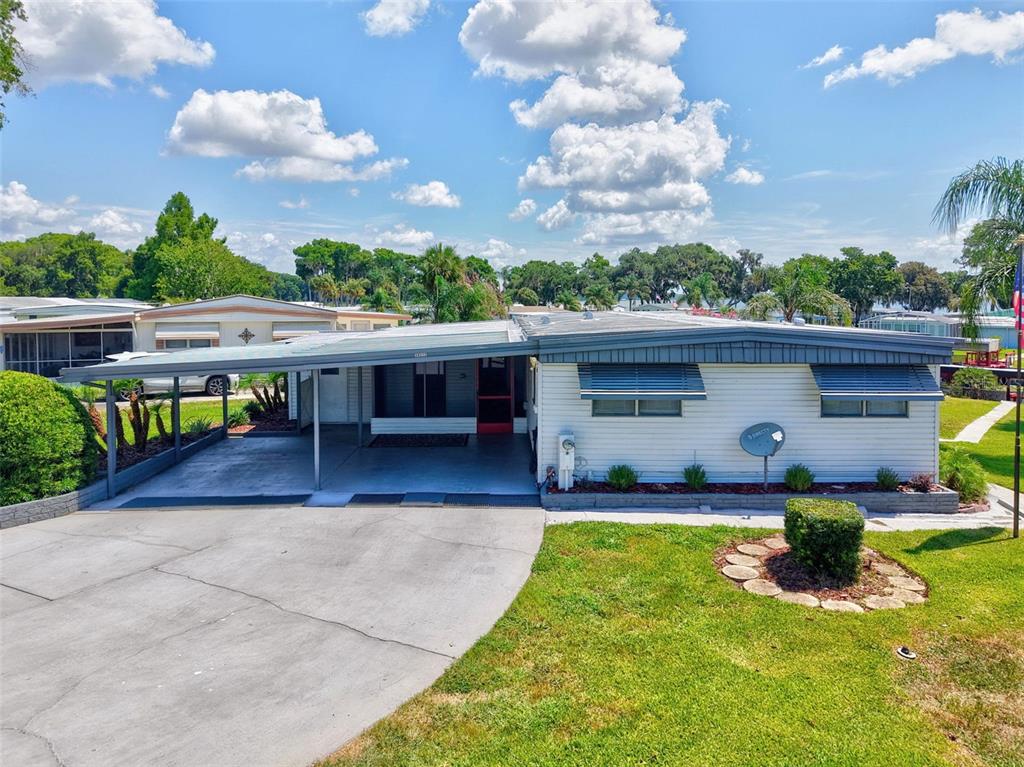 A single-story manufactured home with a carport, concrete driveway, and a small front lawn — 34312 CARL ROAD, LEESBURG, FL