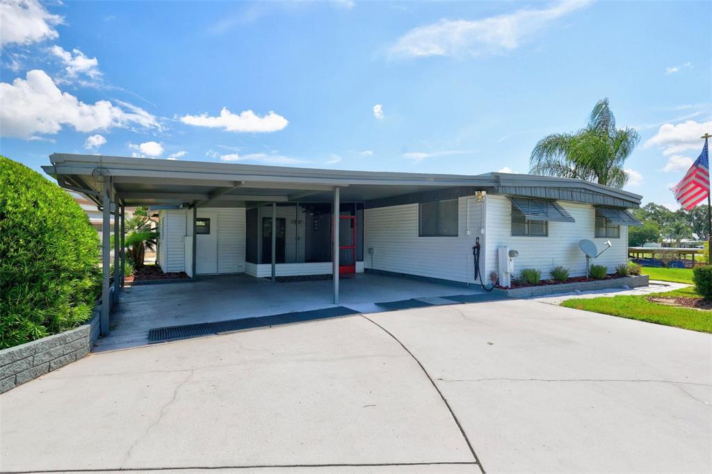 A single-story mobile home with a large carport and a concrete driveway under a blue sky — 34312 CARL ROAD, LEESBURG, FL