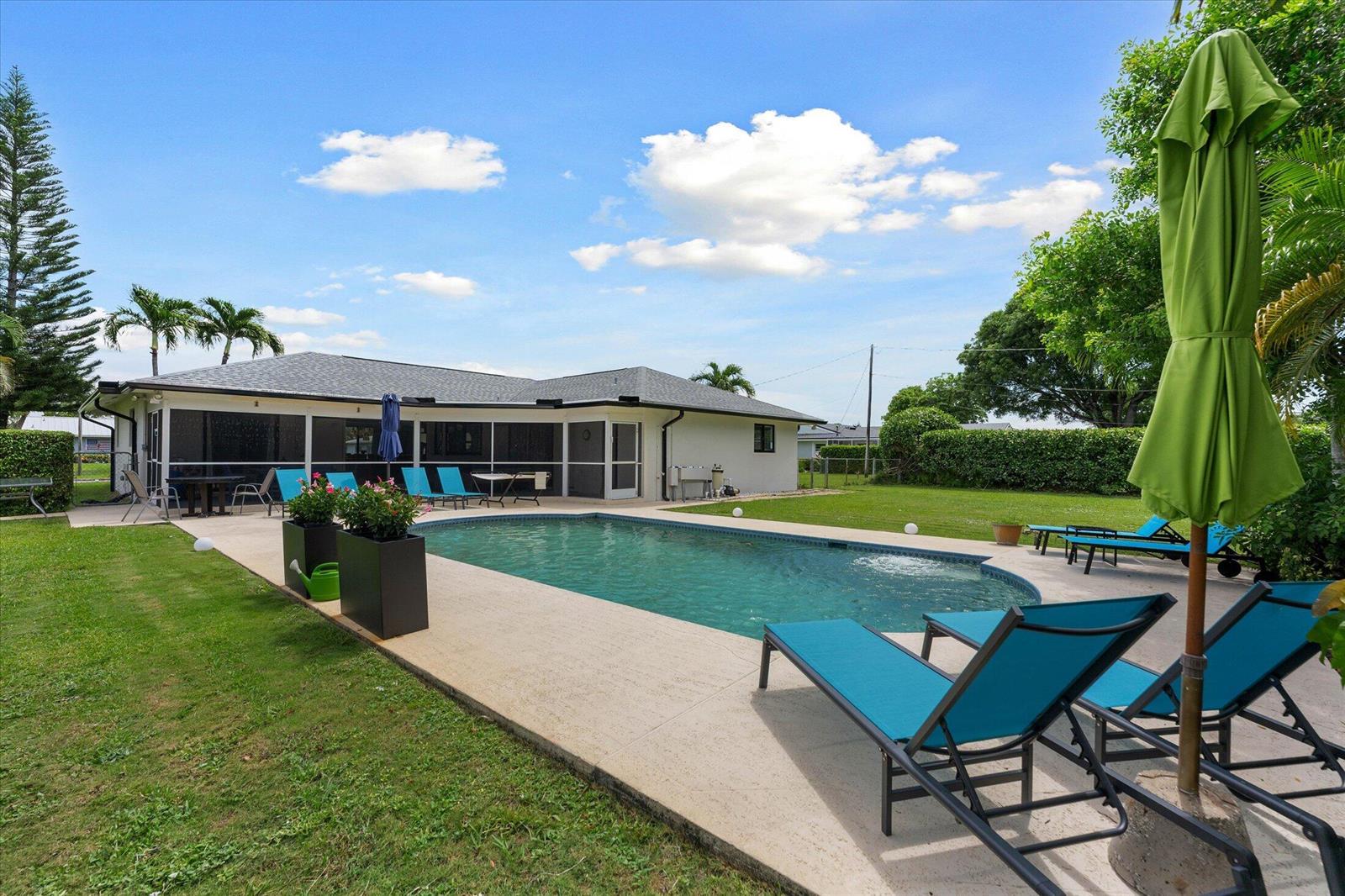 A backyard features a swimming pool, a patio with lounge chairs, and a screened-in porch — 3313 Sherwood Boulevard, Delray Beach FL 33445, DELRAY BEACH, FL