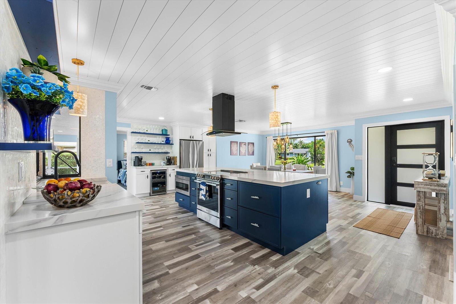 A kitchen features a large blue island, white cabinets, stainless steel appliances, and wood-look flooring — 3313 Sherwood Boulevard, Delray Beach FL 33445, DELRAY BEACH, FL